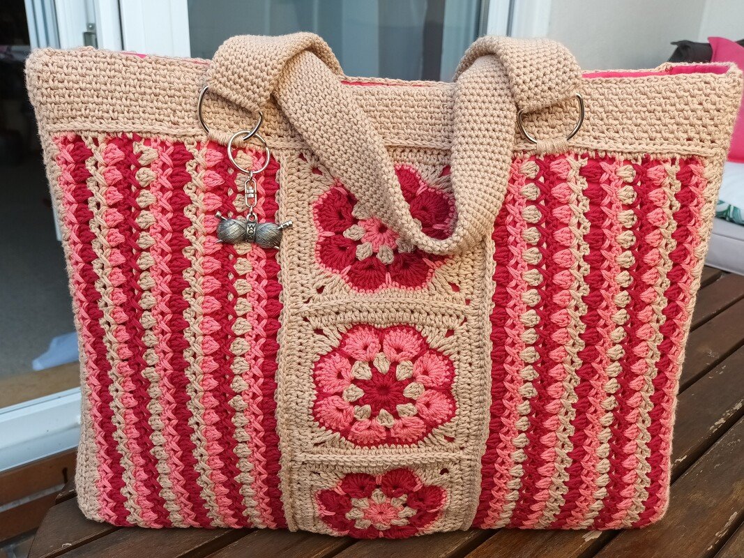 Rechteckiger gehäkelter Shopper in Beige, Rosa und Rot mit drei mittigen Granny-Square-Blumen, gestreiften Seiten, breiten Trägern, rosa Innenfutter und einem Garn-Charm