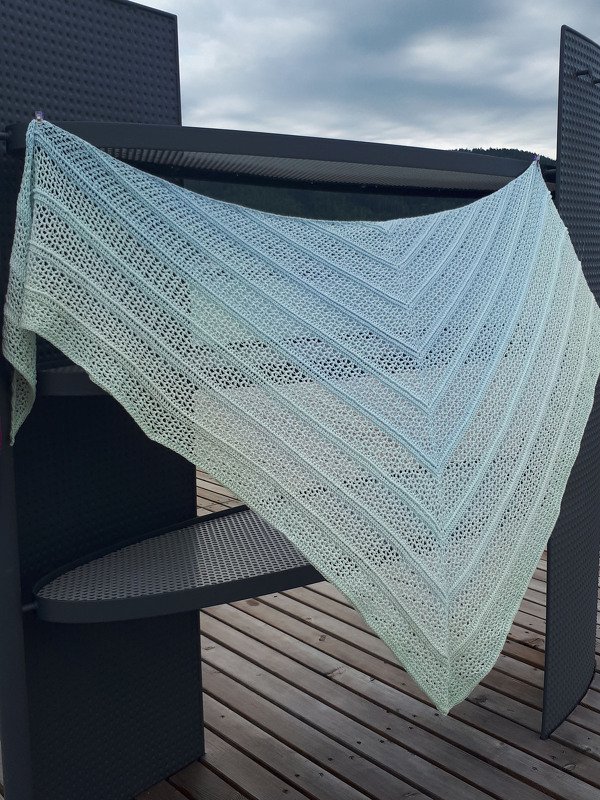 Gehäkeltes Dreieckstuch in Blau‑Grün mit Lochmuster, über einer dunklen Terrassenlehne drapiert