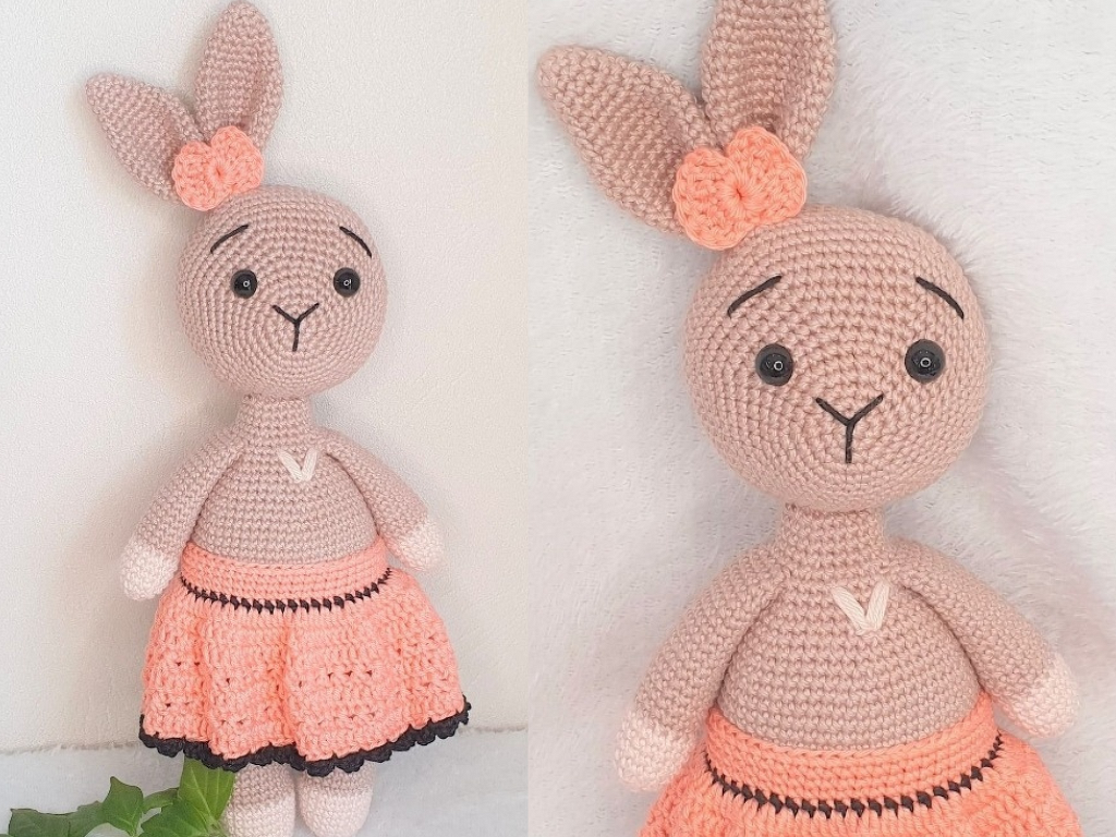 Gehäkelter Amigurumi-Hase in Beige mit lachsfarbenem Häkelrock, schwarzem Saum und Blüte am Ohr
