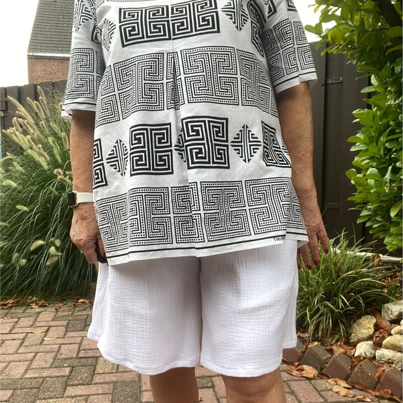 Person in knielangen weißen, weit geschnittenen Shorts und schwarz-weißer gemusterter Tunika, Vorderansicht bis zu den Knien