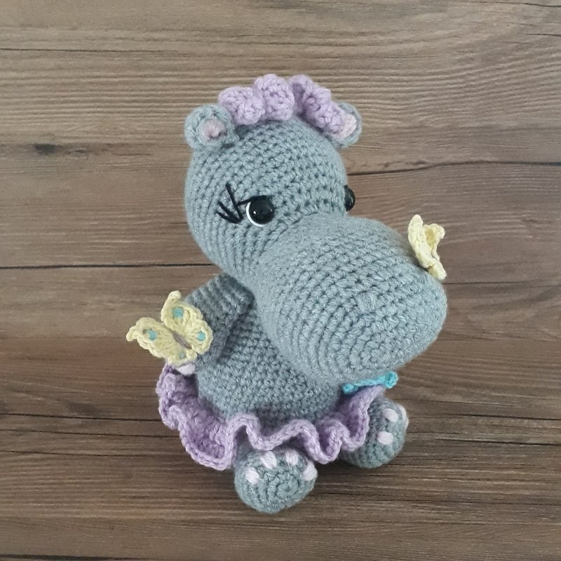 Gehäkeltes graues Amigurumi-Nilpferd mit lila Rüschrock und gelb-blauen Schmetterlingen.