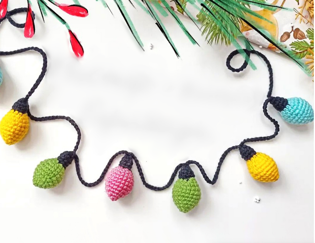 Bunte gehäkelte Lichterkette mit gelben, grünen, pinken und blauen Birnen auf weißem Hintergrund
