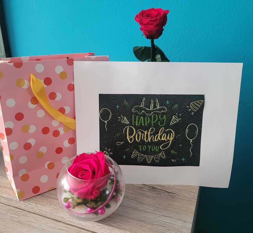 Geburtstagskarte mit dem Schriftzug "Happy Birthday to you" auf dunklem Feld, dekoriert mit Torte, Ballons, Rosen und gepunkteter Geschenktüte.