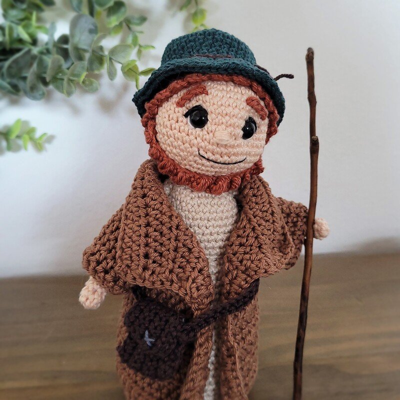 Amigurumi-Krippenfigur: gehäkelter Hirte mit Mantel, Hut, Tasche und Stab.