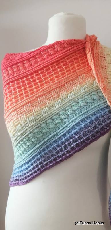 Close-up of a triangle crochet shawl with stitch bands in a rainbow gradient draped on a mannequin