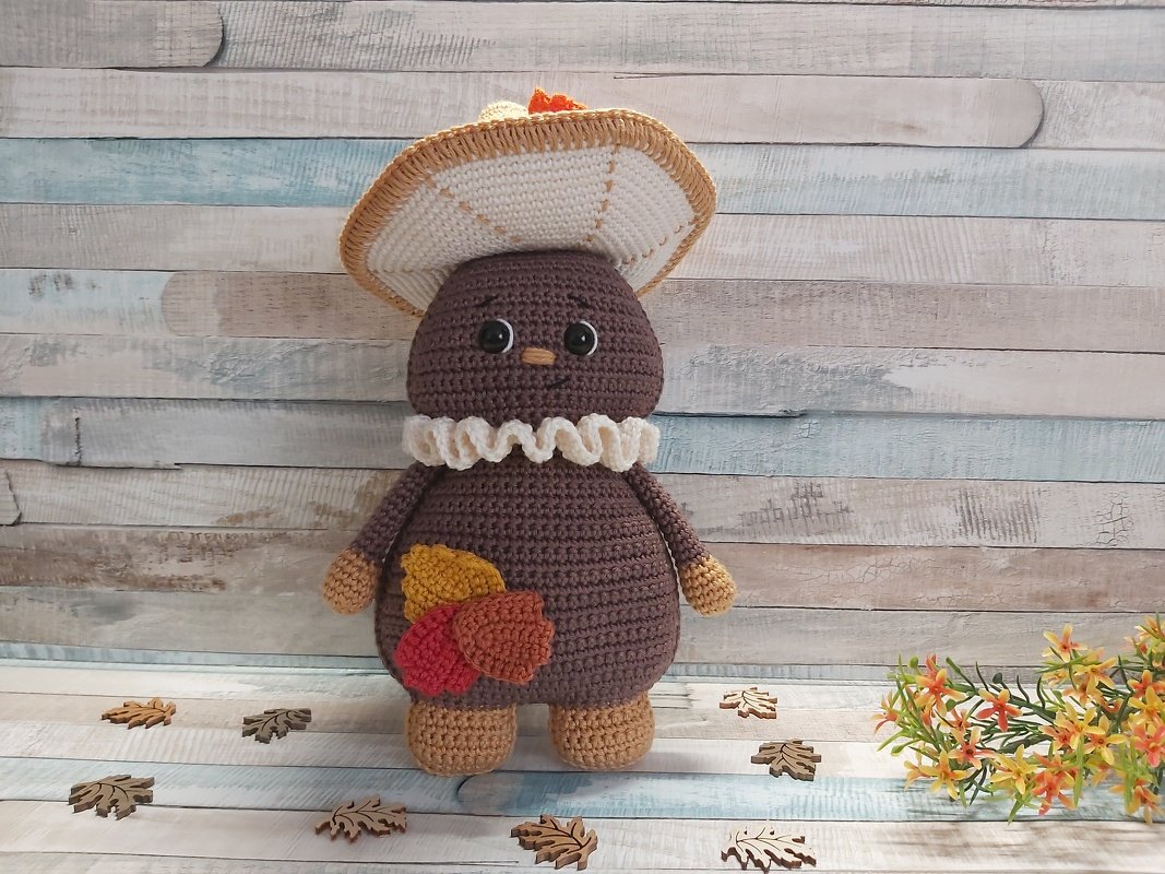 Herbstliche Amigurumi-Figur mit breitkrempigem Hut, weißem Rüschenkragen und Blätter-Applikationen in Rot, Gelb und Braun
