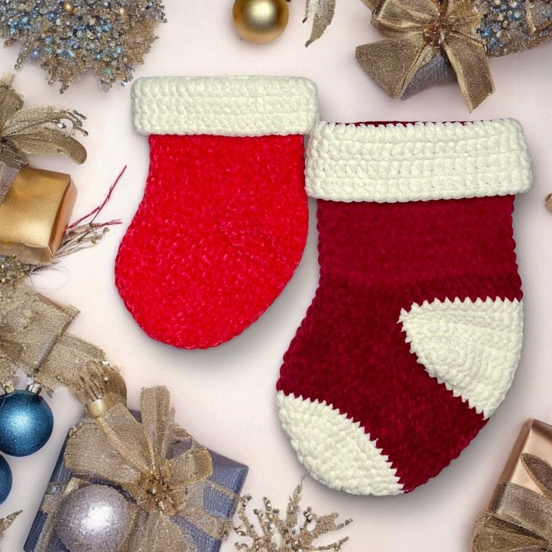 Zwei gehäkelte Weihnachtsstrümpfe in Hell- und Dunkelrot mit umgeschlagenem weißem Bündchen, liegend zwischen Geschenk- und Weihnachtsdekoration