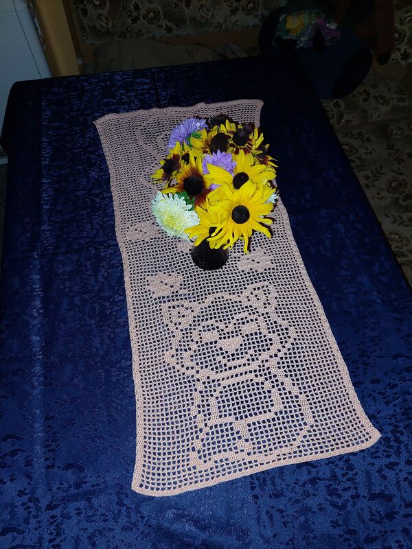 Beiger gehäkelter Tischläufer mit Katzenmotiv auf dunkelblauem Untergrund und Blumenstrauß