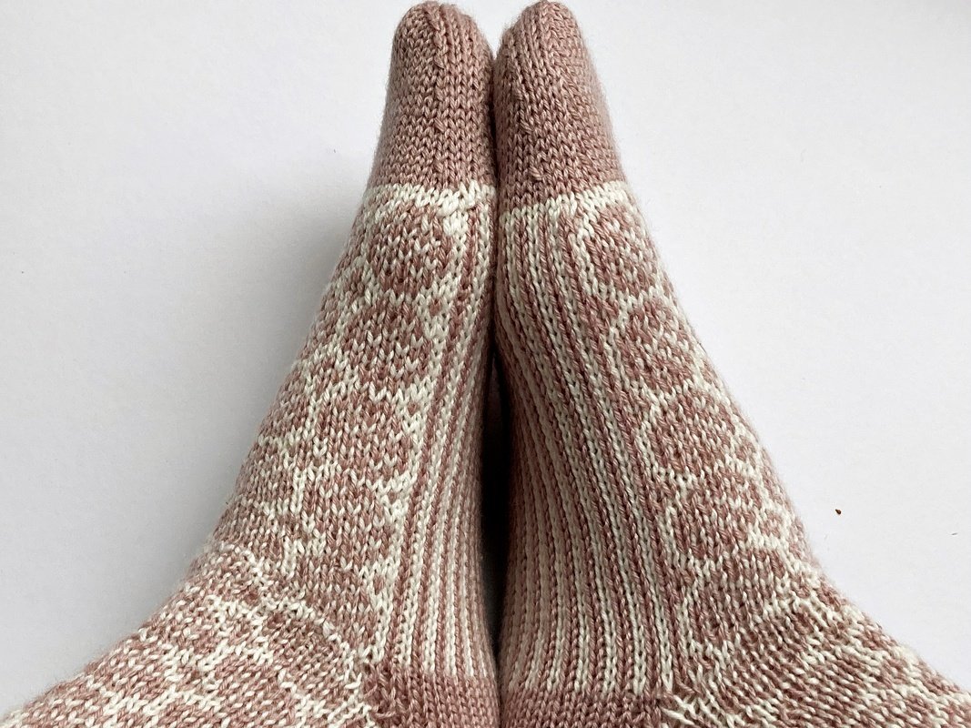 Paar gestrickter Damensocken in Rosé und Creme mit geometrischem Muster, Ansicht von oben