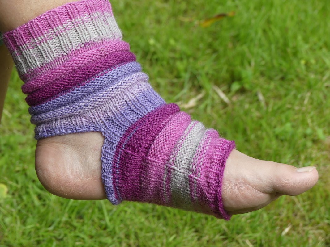 Gestrickte Fußstulpe mit Lila-, Pink- und Graustreifen an einem Fuß auf Gras