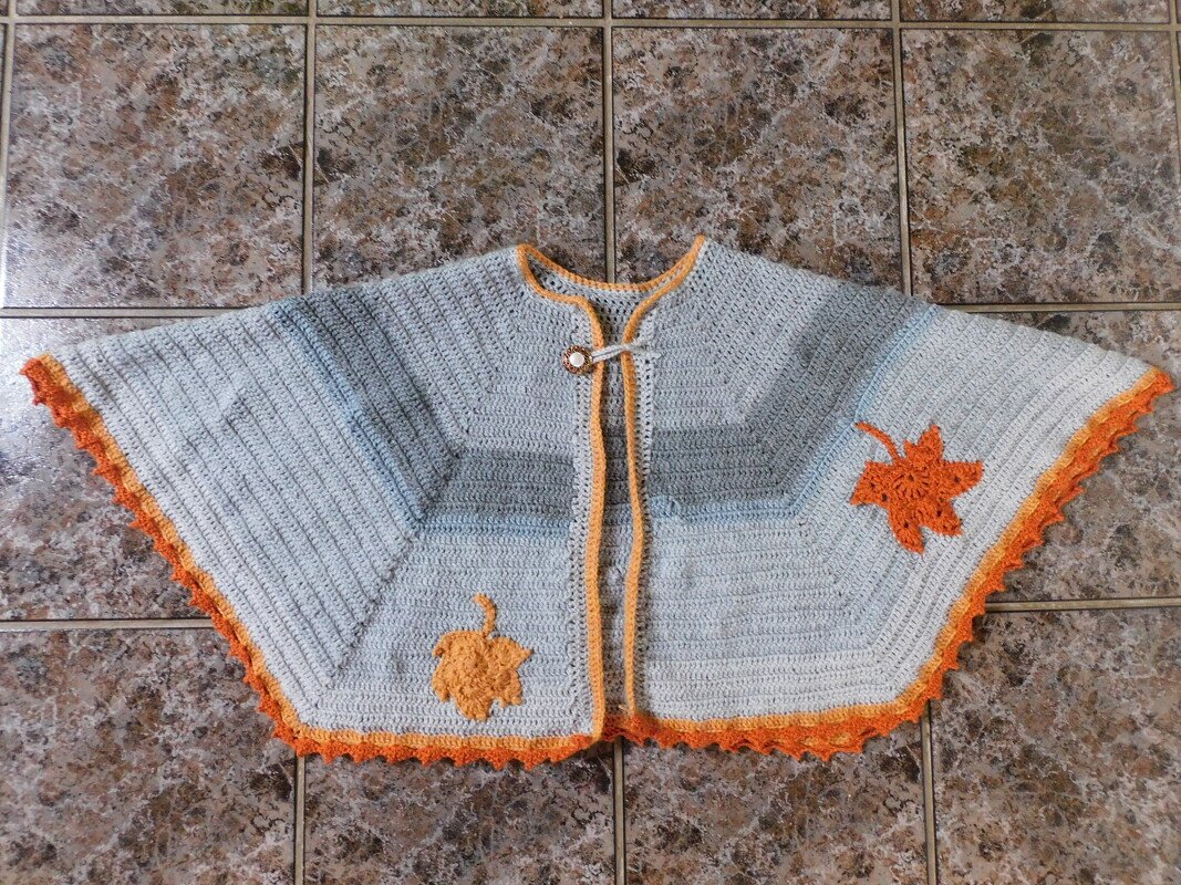 Gehäkelter Damenponcho hellgrau mit orangefarbener Borte und Blatt-Applikationen, liegend