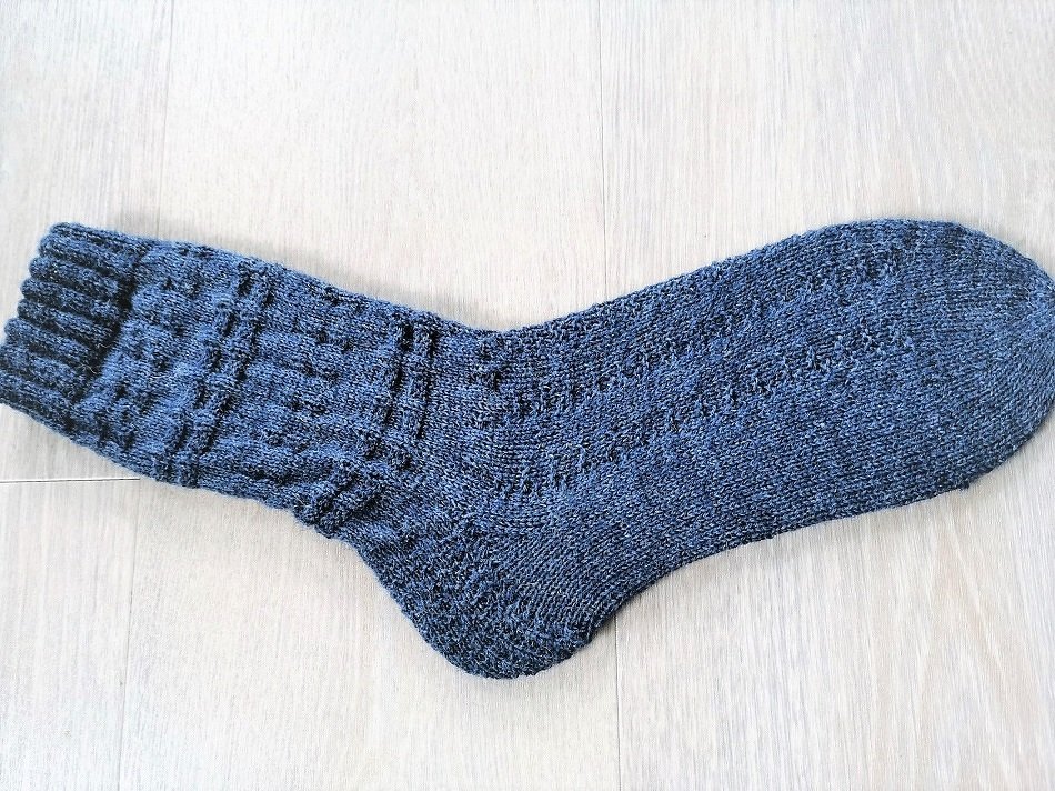Dunkelgraue gestrickte Herrensocke mit Rippenbündchen und Strukturmuster auf hellem Holzuntergrund
