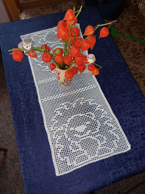 Weißer gehäkelter Tischläufer im Filetmuster mit Eulenmotiven auf dunkelblauer Tischdecke, dekoriert mit Vase, Lampionblumen und kleinen Deko-Eulen