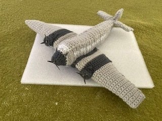 Gehäkeltes graues Amigurumi-Flugzeug mit zwei Propellern auf heller Unterlage