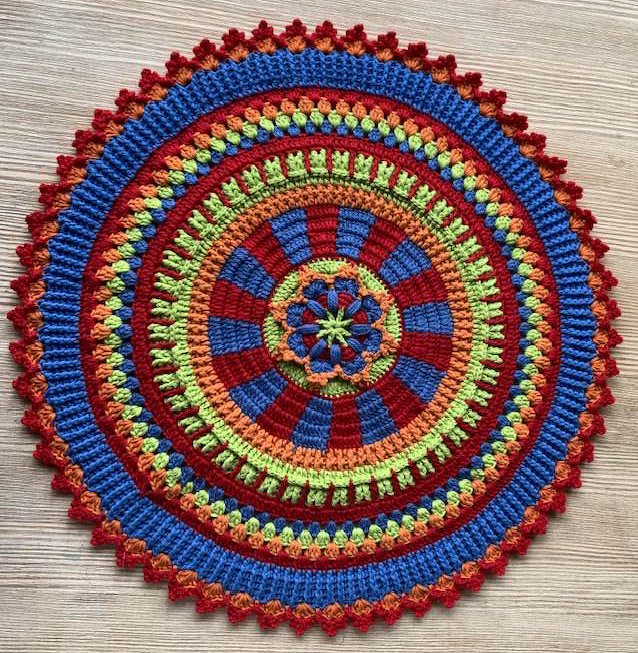 Detailaufnahme eines runden Häkelmusters mit abwechselnden Runden in Blau, Rot, Orange und Grün