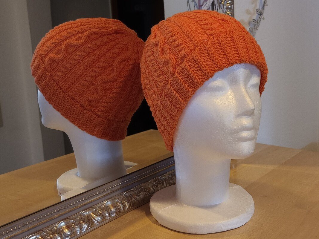 Nahaufnahme einer orangefarbenen gestrickten Mütze mit Zopfmuster auf Styroporkopf