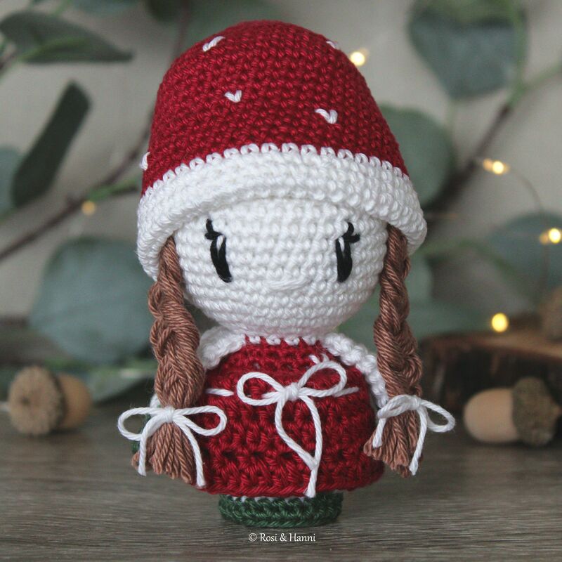 Gehäkelte Amigurumi-Puppe im Fliegenpilz-Design, rote Mütze mit weißen Punkten, rotes Kleid, geflochtene Zöpfe.