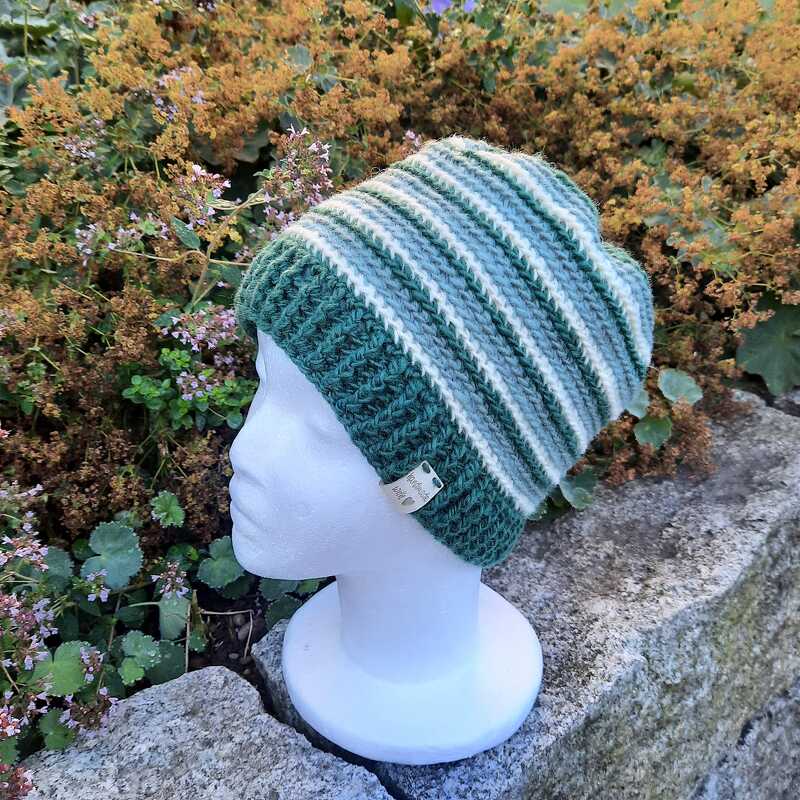 Gehäkelte Beanie mit grünen und weißen Streifen auf weißem Schaufensterkopf vor Pflanzen