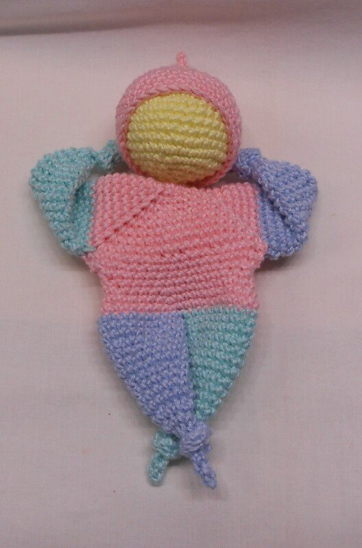 Handgehäkelte Amigurumi-Puppe in Pastellfarben mit geknoteten Enden auf hellem Hintergrund.