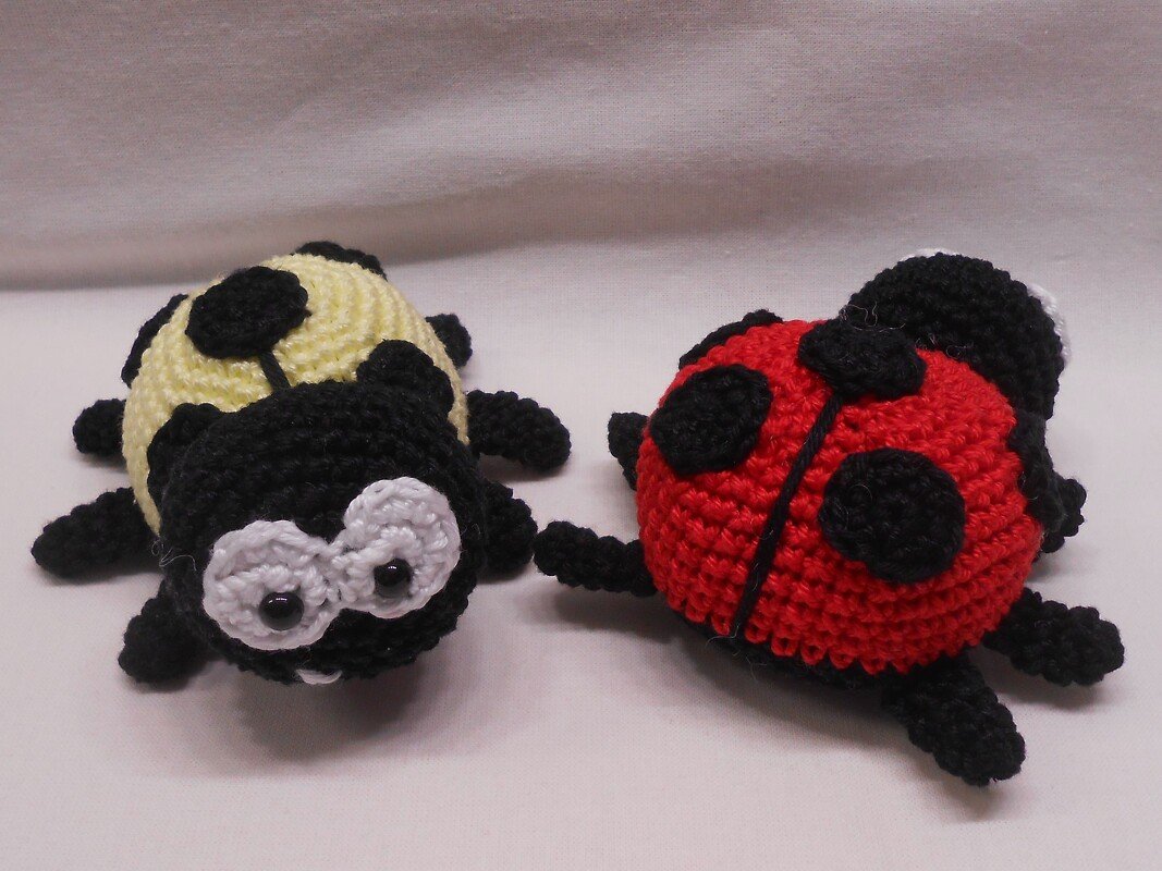 Zwei gehäkelte Amigurumi-Marienkäfer, einer rot mit schwarzen Punkten, einer gelb mit schwarzen Punkten