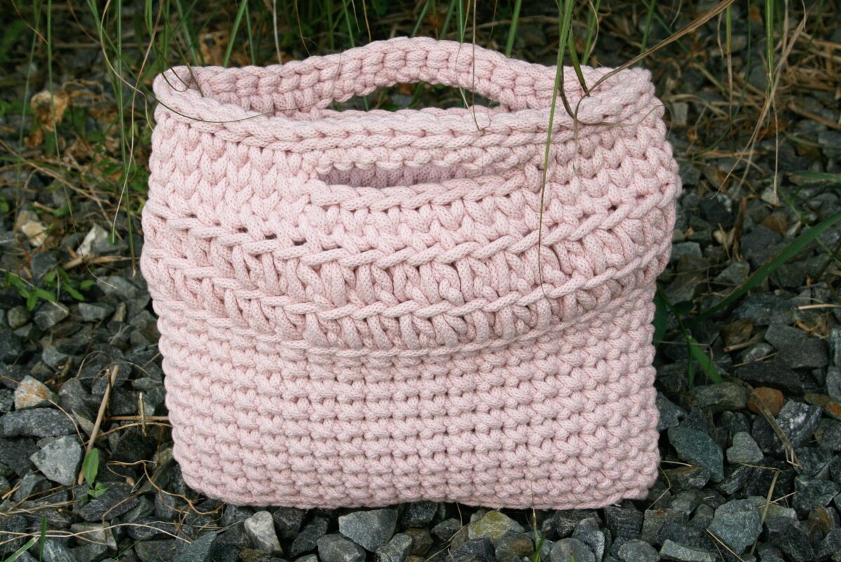 Gehäkelte rosafarbene Henkeltasche mit festen Henkeln auf grauem Schotter