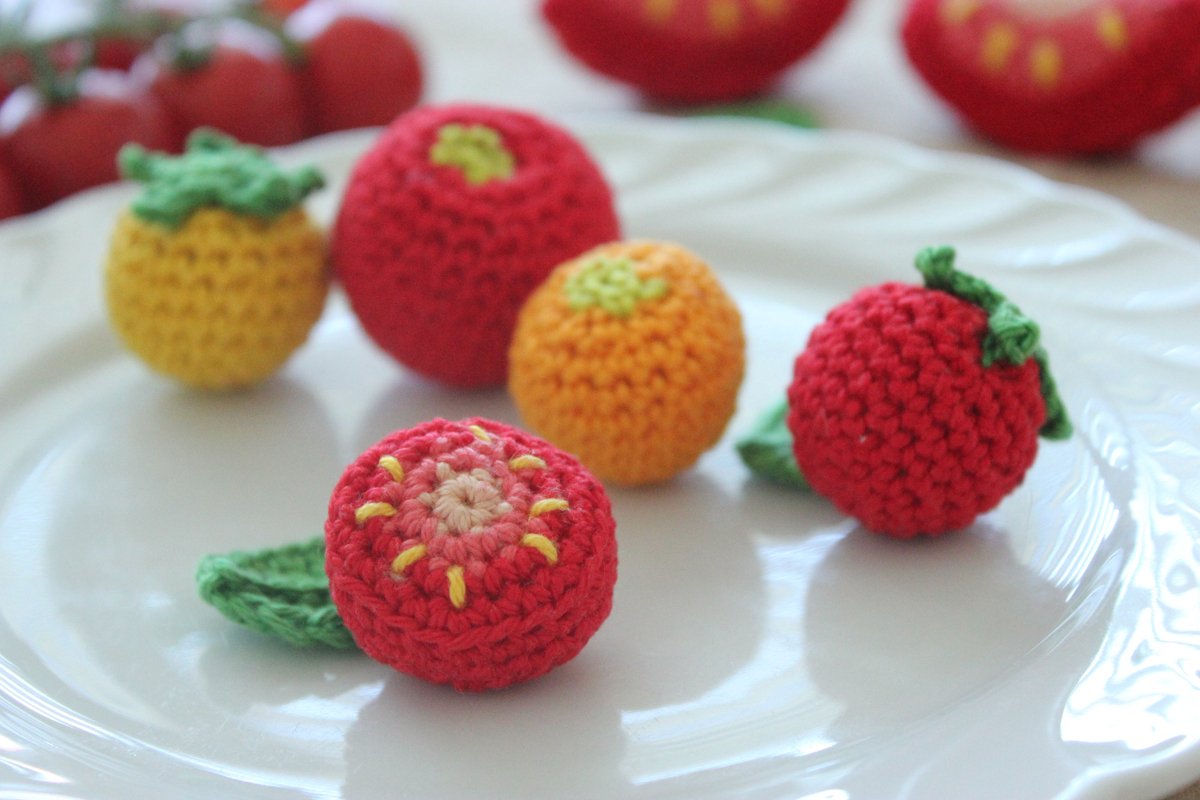 Bunte gehäkelte Früchte und Gemüse (Erdbeere, Orange, Tomate) auf weißem Teller, detailreich.