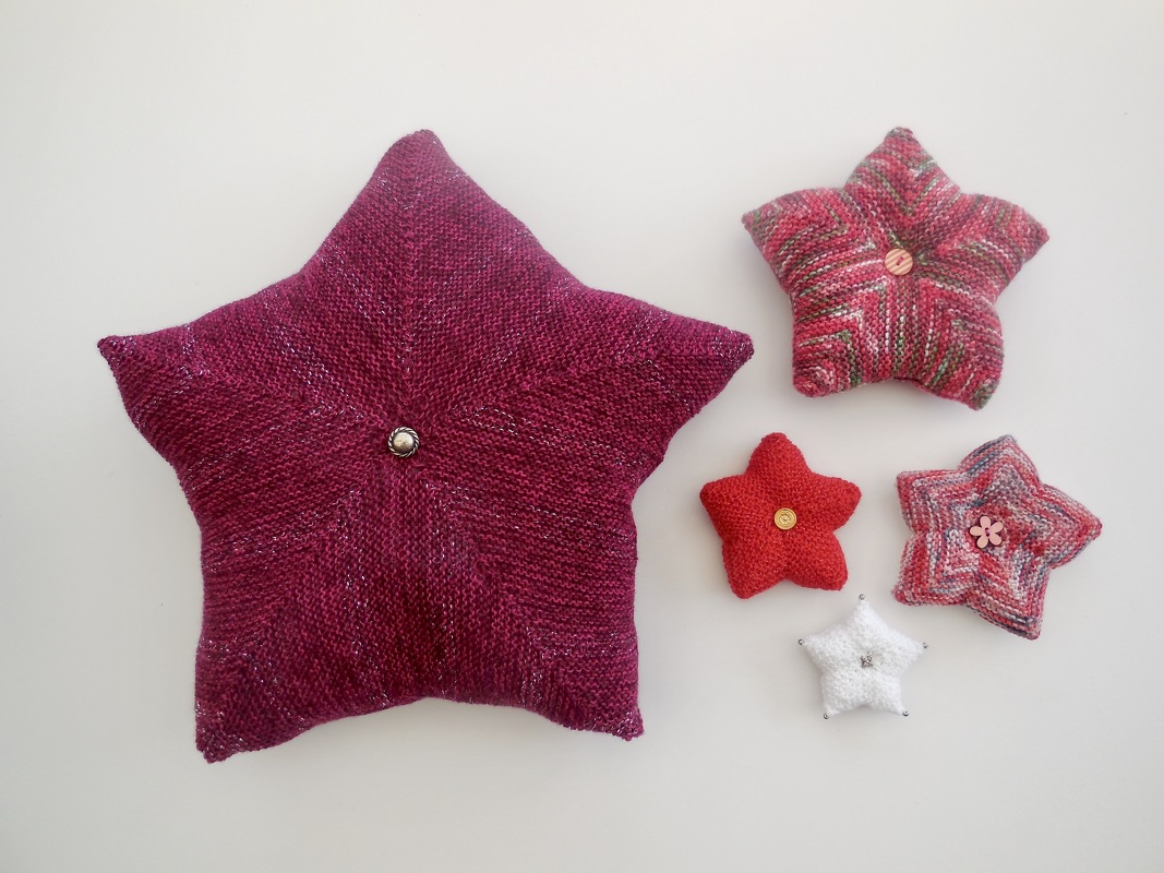 Fünf gestrickte Sternkissen in Pink, Rot und Weiß mit Knöpfen auf hellem Hintergrund