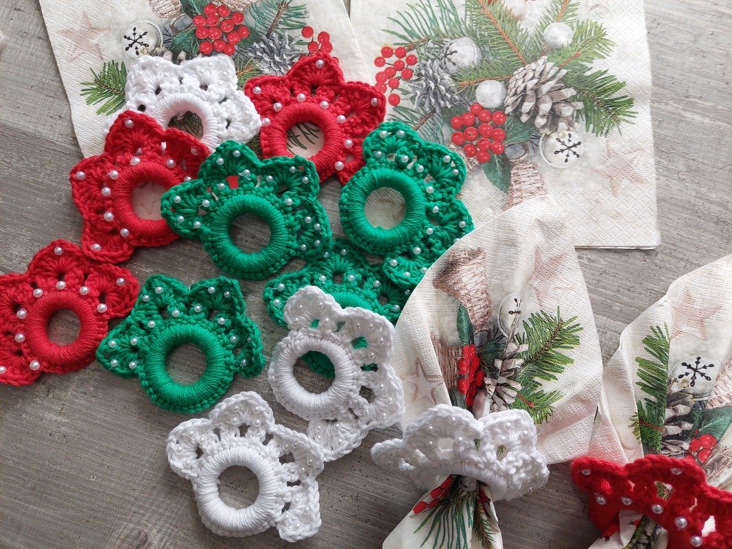 Gehäkelte Serviettenringe in Rot, Grün und Weiß mit Perlen auf weihnachtlichen Servietten und Holzuntergrund.
