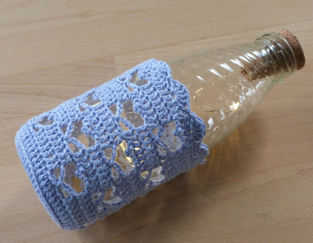 Windlicht aus Glasflasche mit hellblauer Häkelhülle und Lichterkette