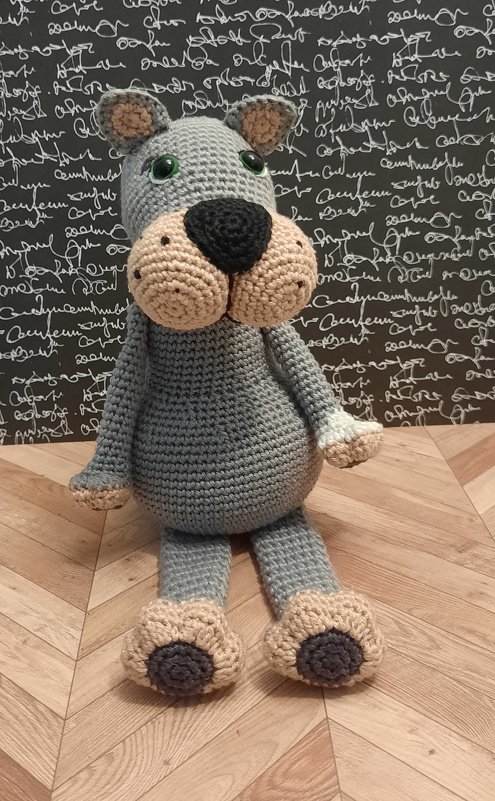 Sitzender gehäkelter grauer Hund mit grünen Augen und beiger Schnauze