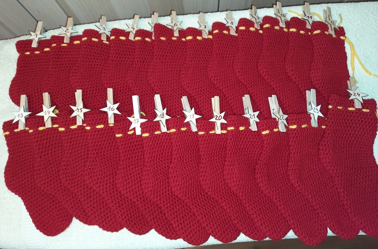 24 rote gehäkelte Säckchen als Adventskalender mit nummerierten Holzstern-Klammern und gelbem Zierband.