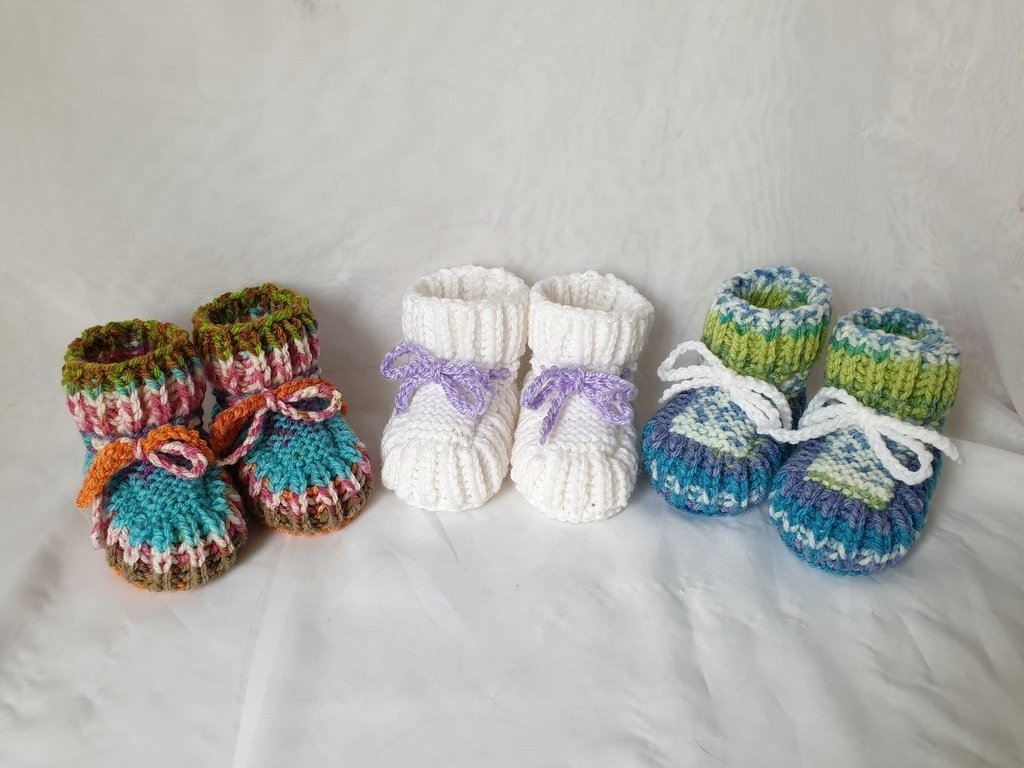 Drei gestrickte Babyschuhe mit Umschlagbündchen und Bindebändern in verschiedenen Farben