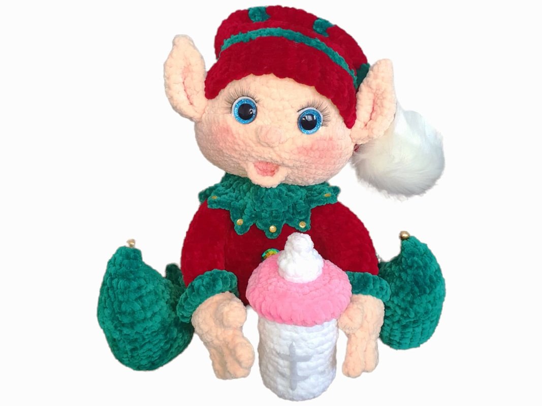Red and green crocheted elf amigurumi holding a pink-topped bottle