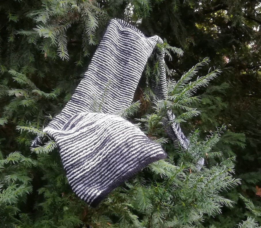 Schwarz-weißer gestrickter Schal mit Streifenmuster an einem Nadelbaum
