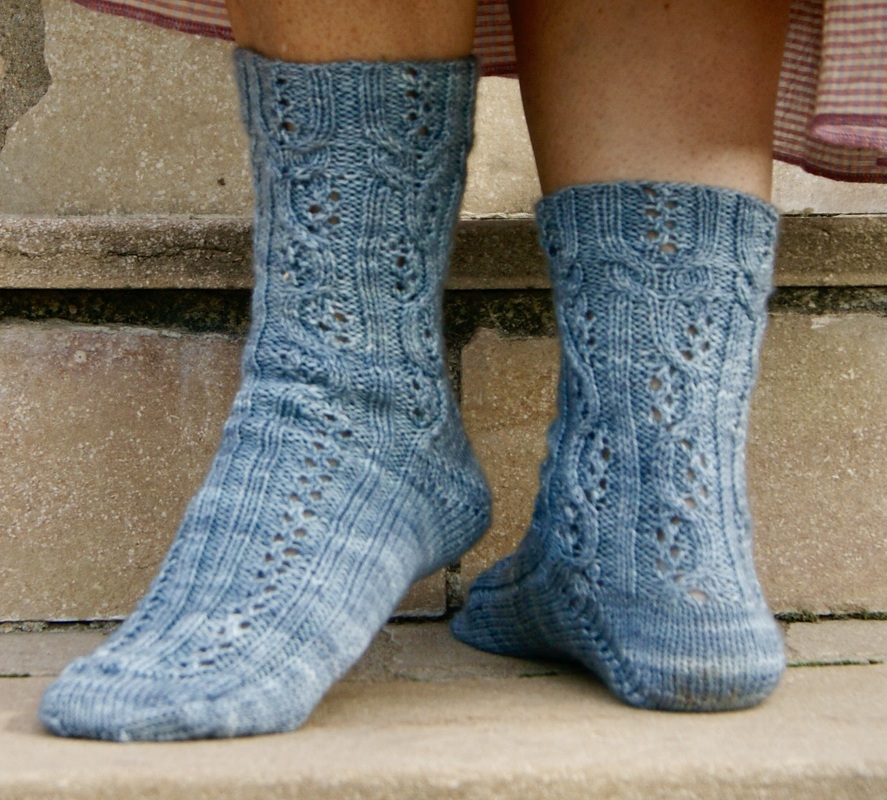 Füße mit hellblauen, handgestrickten Damensocken mit Ajourmuster auf Steinstufen