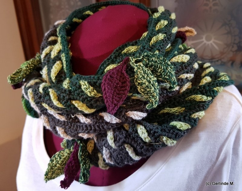 Green, gray, and burgundy crocheted cowl with leaf appliqués on a mannequin.