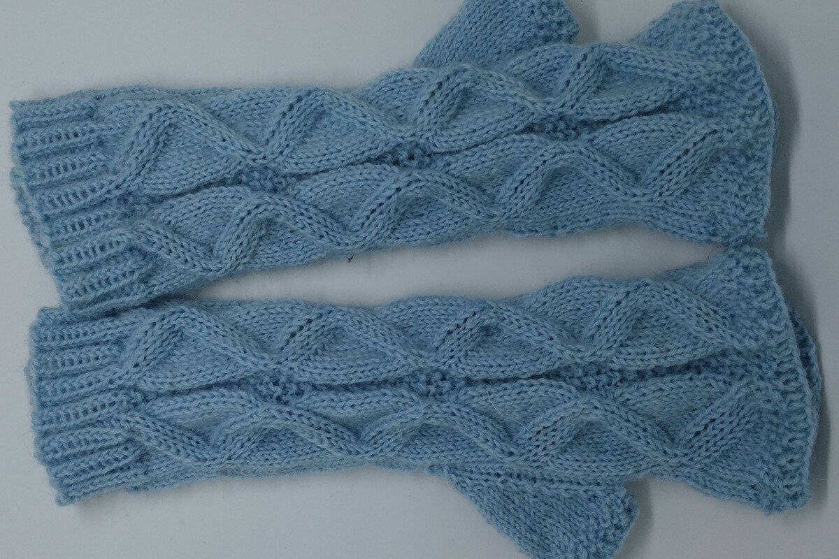 Hellblaue gestrickte Armstulpen mit Zopfmuster und Rippbündchen, liegend.
