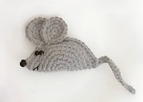Grau gehäkelte Amigurumi-Maus mit großen Ohren, Perlenaugen, schwarzer Nase und gedrehtem Schwanz auf hellem Hintergrund