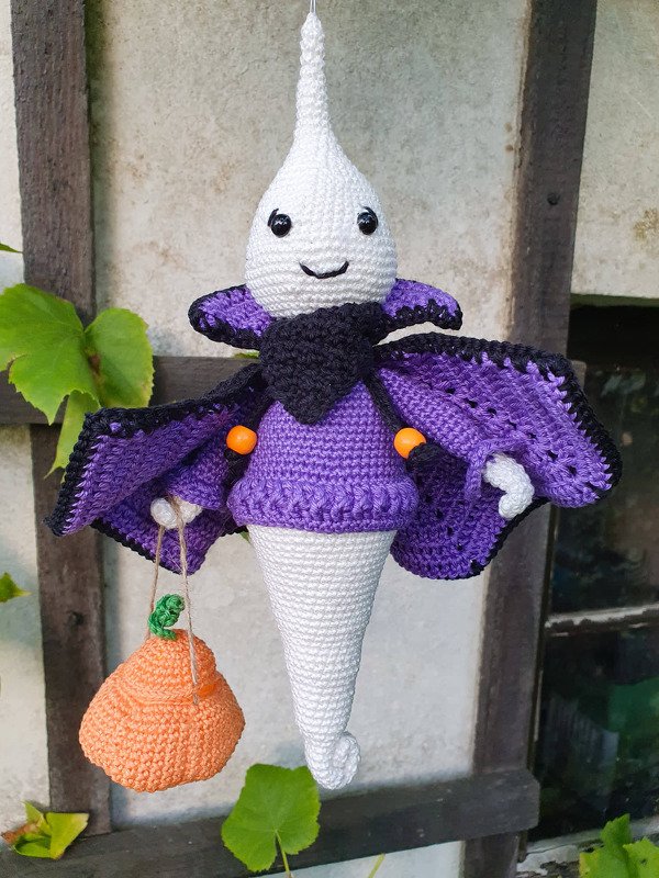 Gehäkeltes Geist-Amigurumi mit lila Umhang und orangefarbenem Kürbisbeutel, hängend