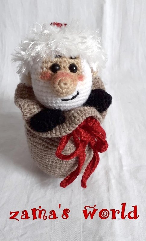 Nahaufnahme eines gehäkelten Wichtels mit weißem Haar in einem beigen Sack mit roter Kordel.
