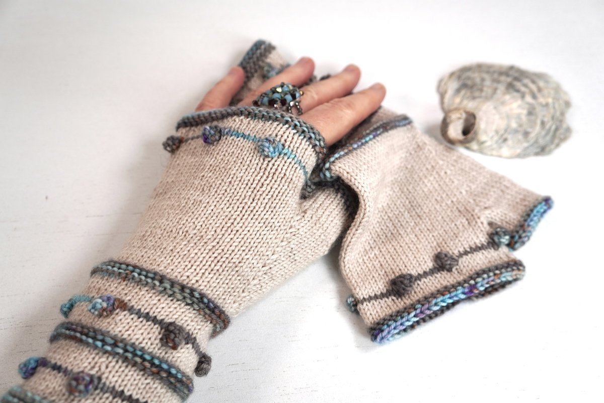 Light beige fingerless knitted gloves with blue, teal and gray stripes and small bobble stitch accents.
