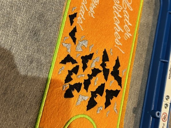 Stickerei auf orangefarbenem Filz mit schwarzen und silbernen Fledermäusen und grünem Rand