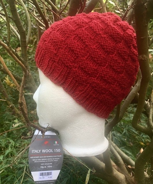 Rote gestrickte Mütze mit Strukturmuster auf weißem Kopfmodell vor Zweigen