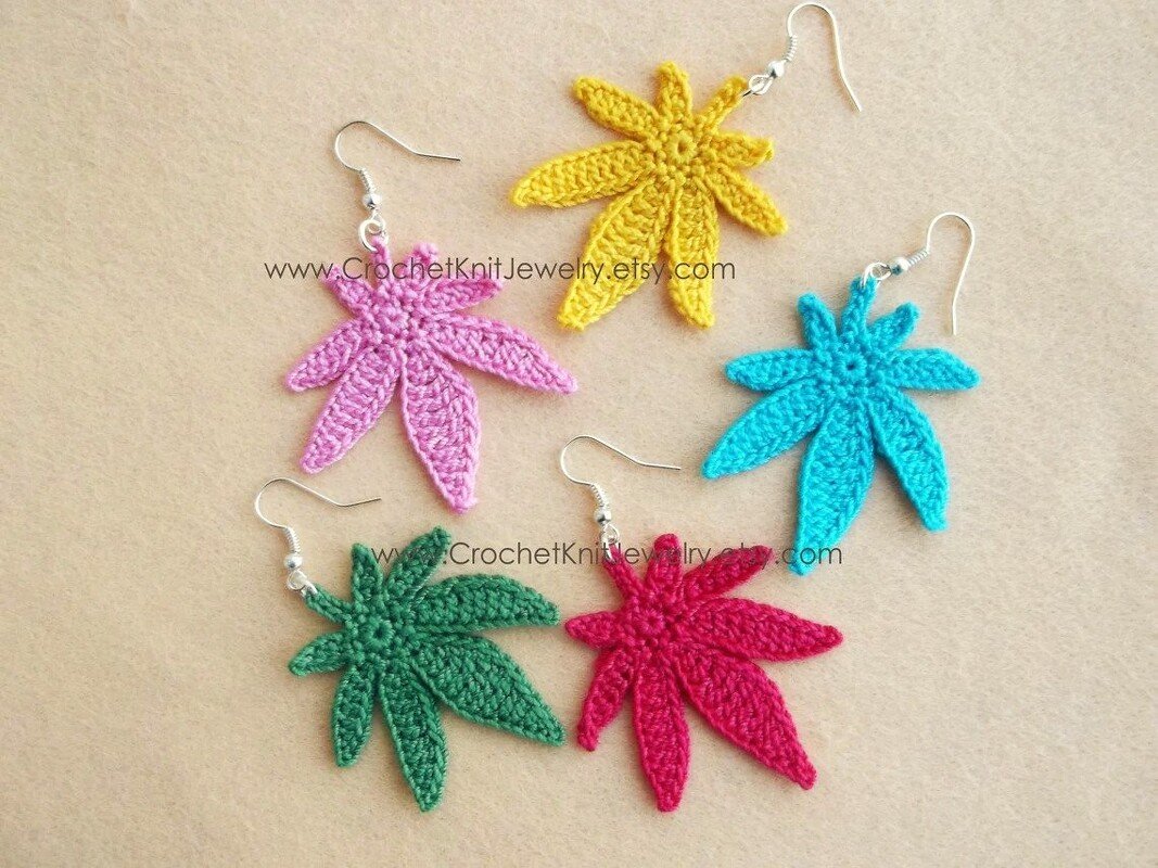 Five handmade crochet leaf dangle earrings in pink, yellow, blue, green and red on a beige surface.