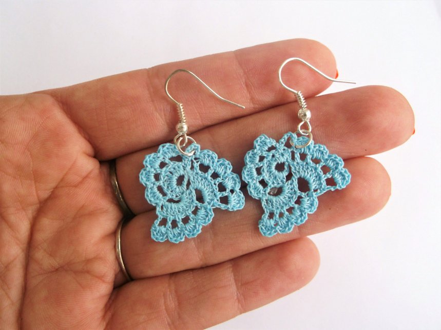 Pair of small light-blue crochet lace earrings on hooks held in a hand to show scale