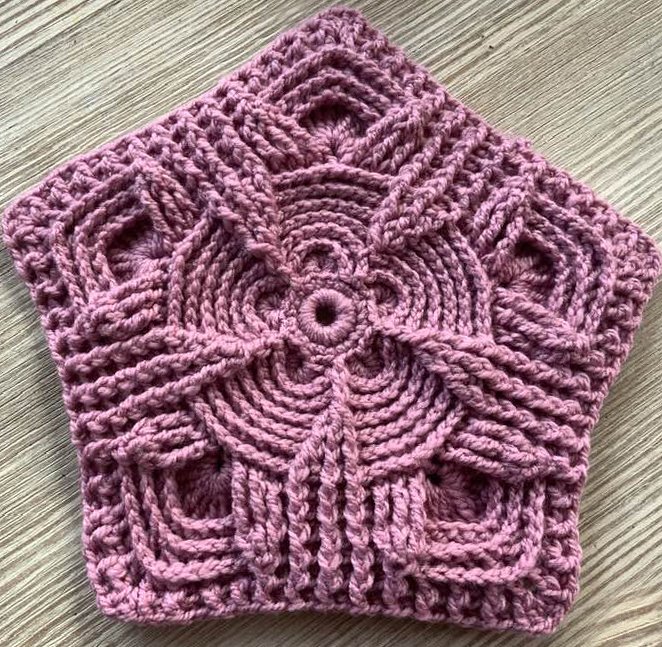 Altrosa gehäkeltes Fünfeck mit plastischem Reliefmuster auf hellem Holzuntergrund