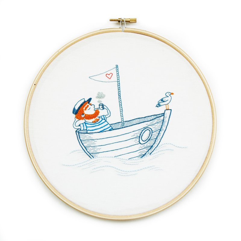 Gesticktes Motiv eines Seemanns mit Pfeife im Boot, mit Möwe und Herzflagge im Stickrahmen.
