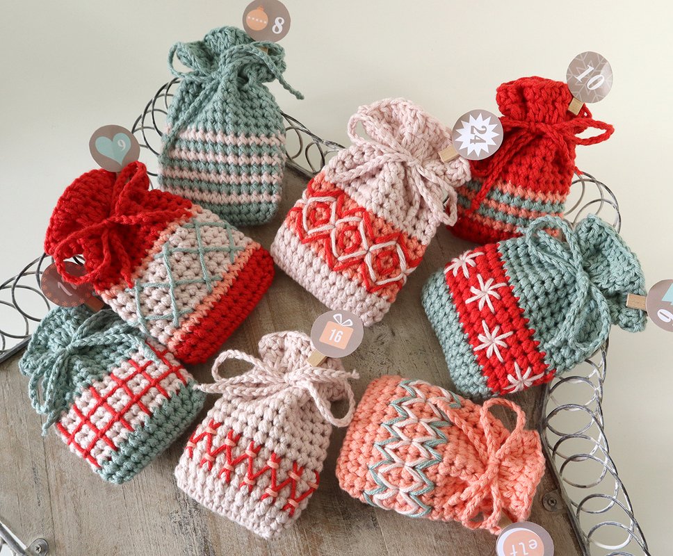 Mehrere gehäkelte Adventskalendersäckchen in verschiedenen Farben und Mustern auf einer Holzoberfläche.