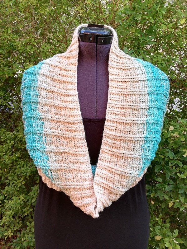 Gehäkelter creme- und türkisfarbener Loop-Schal mit strukturierter Blockoptik auf Schneiderpuppe