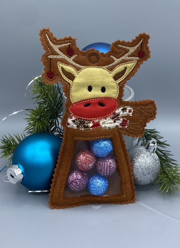 Braune Rentier-Tasche aus Stoff mit transparentem Fenster, gefüllt mit bunten Schokokugeln, vor Weihnachtskugeln